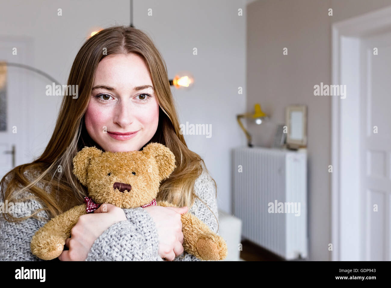 Porträt von Mitte Erwachsene Frau im Wohnzimmer umarmt Teddybär Stockfoto