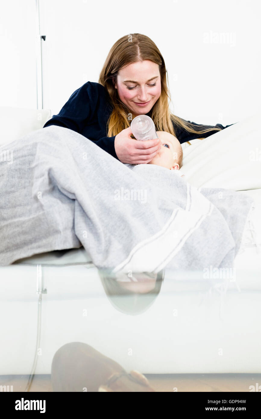 Mitte Erwachsene Frau Babyflasche Baby Tochter auf sofa Stockfoto