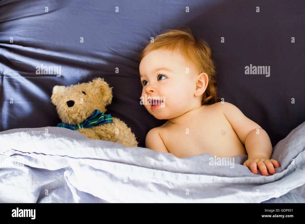 Babymädchen mit Teddybär im Bett liegend Stockfoto