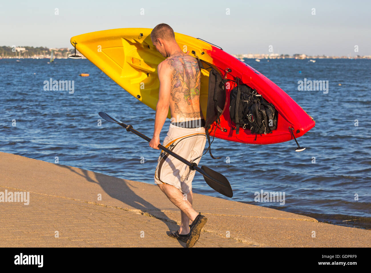 Mann mit Tattoos auf Rücken mit Kajak, nach Kajak rund um den Hafen von Poole im Juli Stockfoto