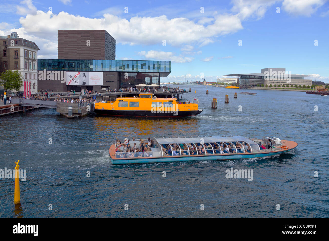 Ein Kanalkreuzfahrtschiff und ein gelber Hafenbus am Royal Playhouse in Nyhavn in Kopenhagen. Das Royal Danish Opera House befindet sich gegenüber vom Hotel. Stockfoto
