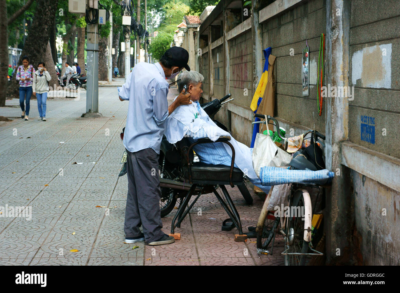 Traditionelle Lebensweise der armen Menschen in Asien urban, vietnamesische männliche Friseur Arbeit im Freiluft-Shop auf Bürgersteig Stockfoto