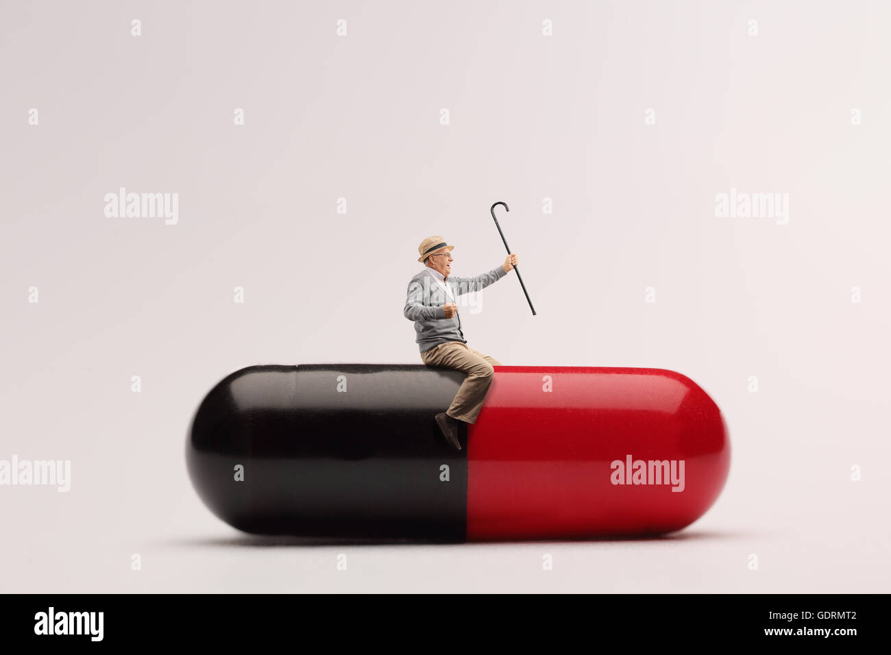 Reifer Mann sitzt auf einem riesigen Pille und halten einen Spazierstock Stockfoto