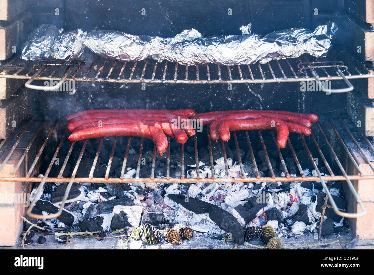 Nahaufnahme von einem Grill mit Würstchen und Folie eingewickelt Bratkartoffeln auf dem grill Stockfoto
