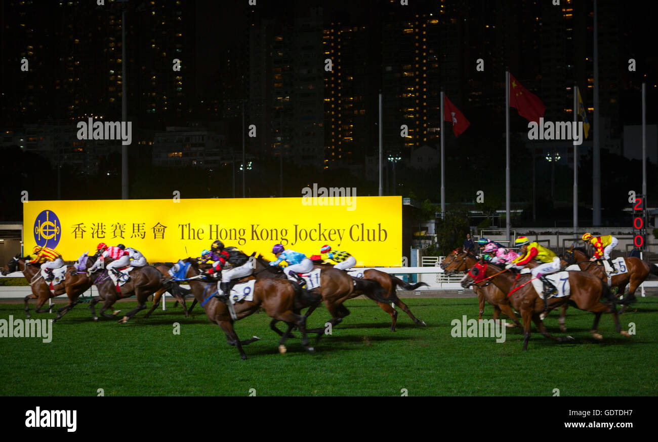 Pferde Rennen vorbei an dem Schild an der Hong Kong Jockey und Club Happy Valley Racecourse in Hong Kong. Stockfoto