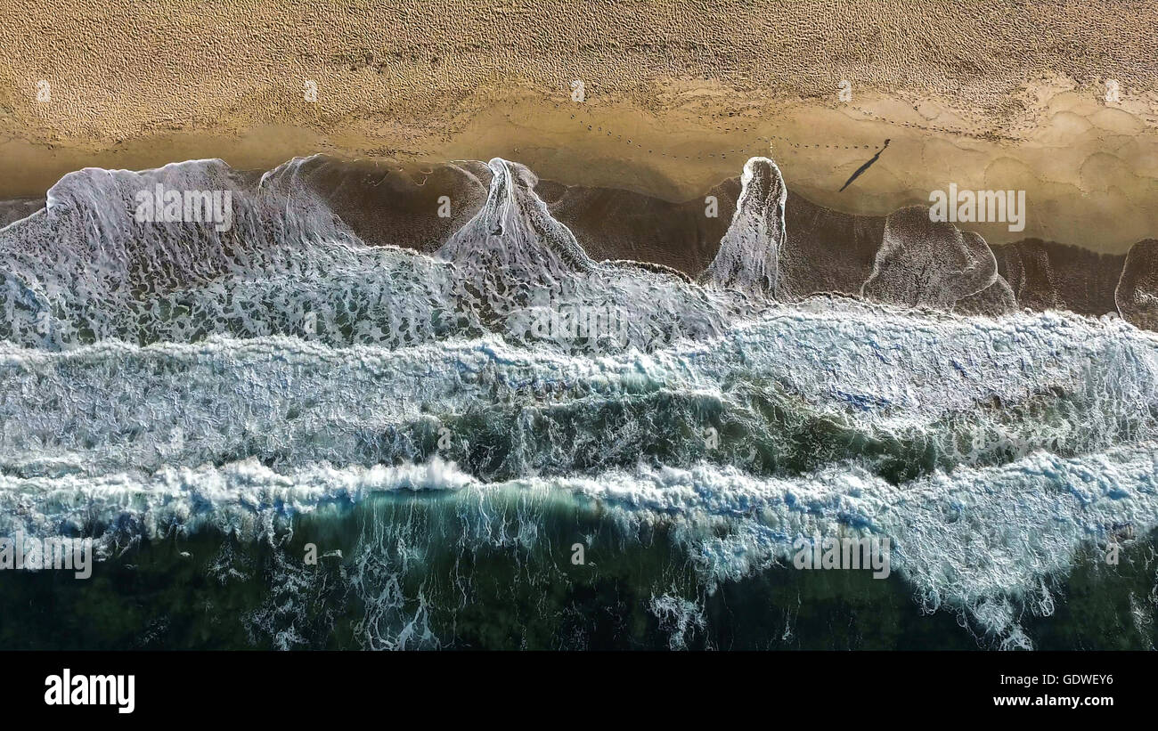 Luftaufnahme des Gehens Mann an einem Strand mit Wellen brechen. Stockfoto