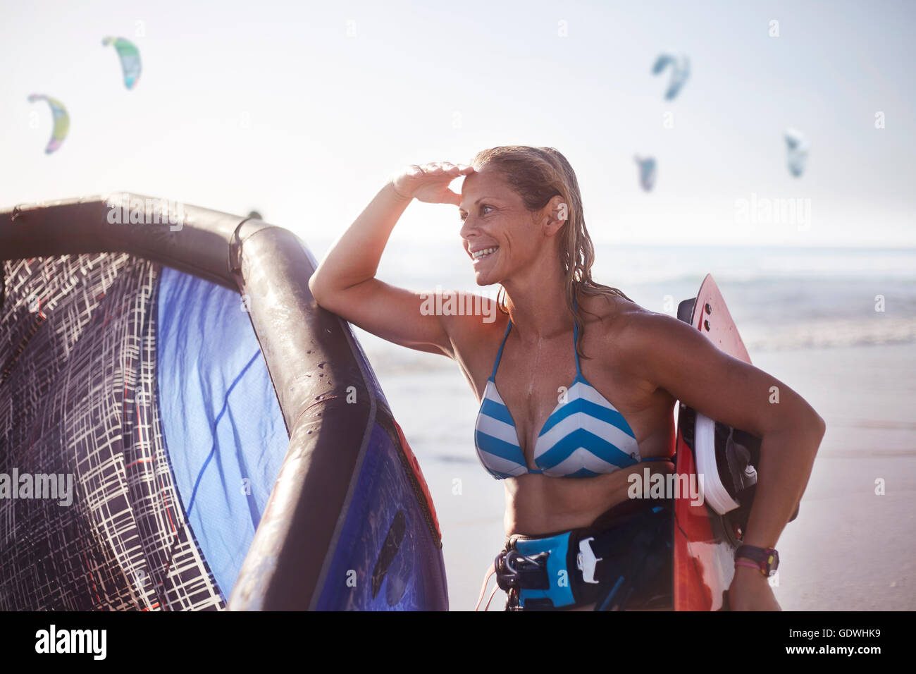 Lächelnde Frau mit Kiteboard Ausrüstung am Strand Stockfoto