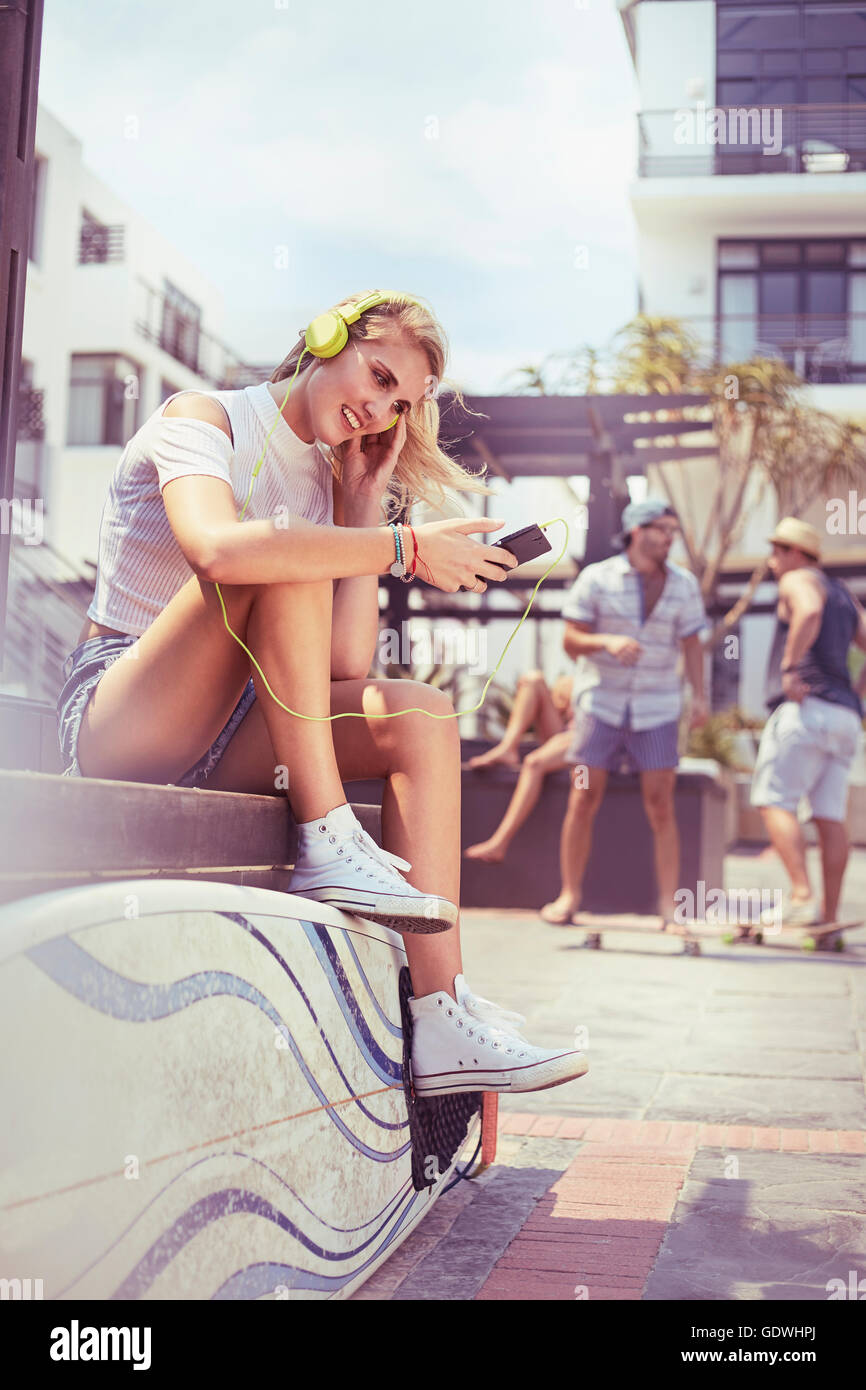 Junge Frau mit Kopfhörer und MP3-Player anhören von Musik mit Surfbrett Stockfoto