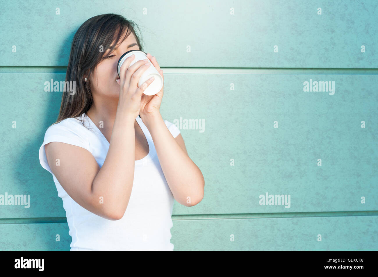 Junge Frau Kaffeetrinken von Take-away-Becher außerhalb auf grüne Wand mit Kopie Bereich Werbung Stockfoto