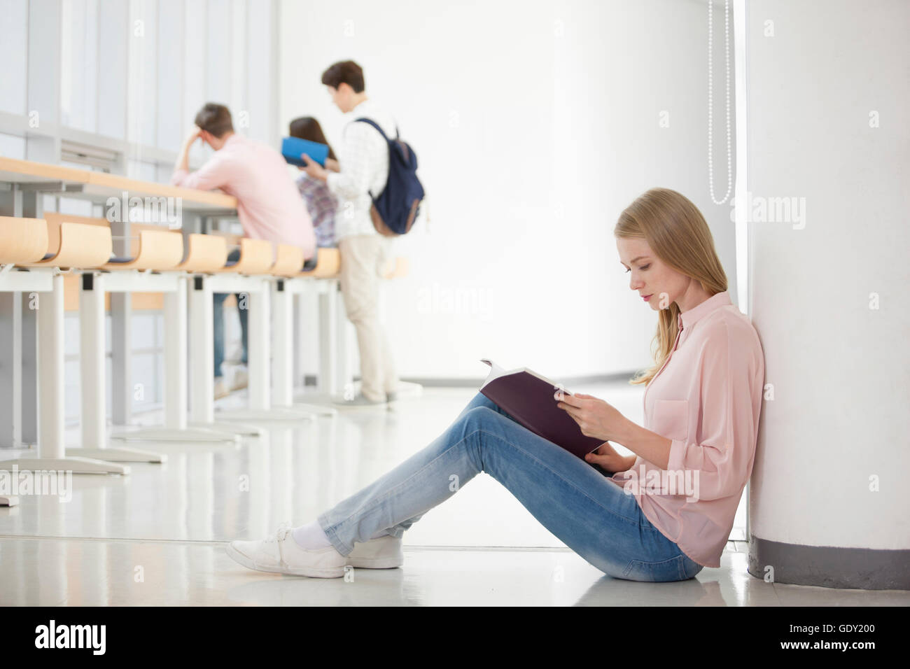 Seitenansicht der junge weibliche Studentin sitzen und lesen und blickte mit drei College-Studenten in Bibliothek Stockfoto