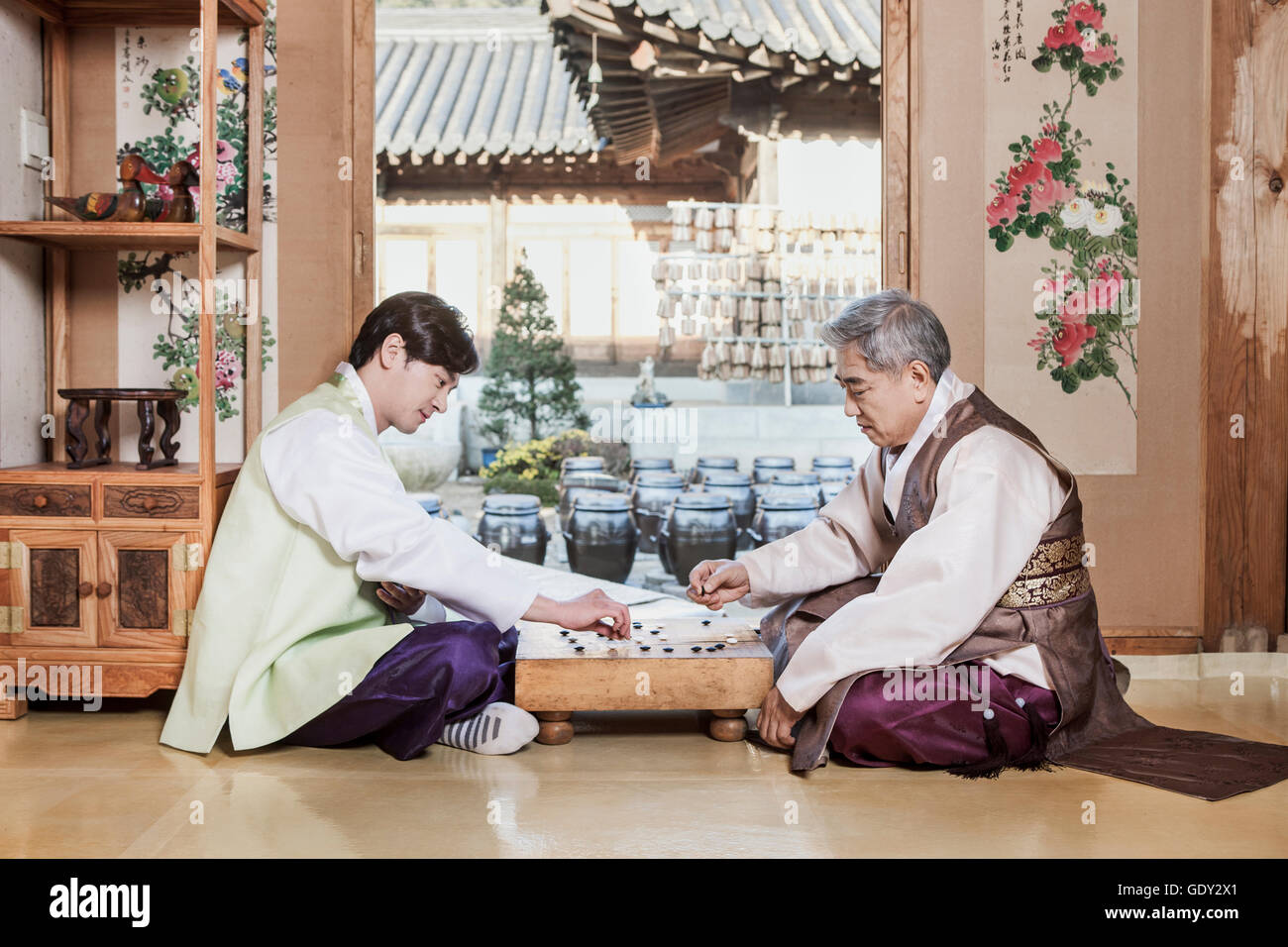 Lächelnder junger Mann und Greis in traditionelle koreanische Kleidung spielen baduk Stockfoto