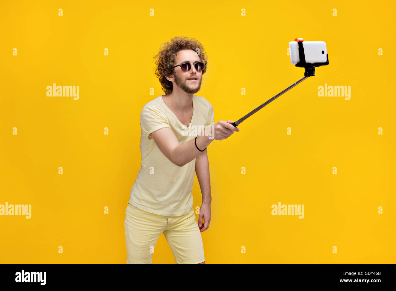 Stilvolle lockige Mann unter Selfie mit Einbeinstativ Stockfoto