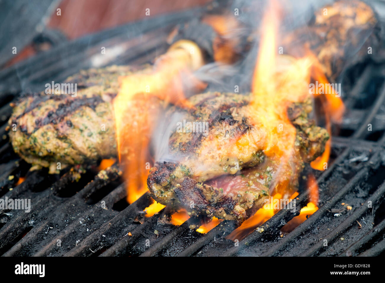 Große Steaks auf dem Grill mit Maiskolben in den Hintergrund, Flammen und Rauch steigt vom grill Stockfoto