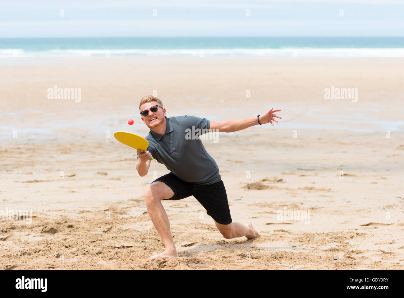 Ein junger Mann eine Schläger und Ball-Spiel zu spielen, an einem Strand Casula Kleidung im Sommer UK Stockfoto