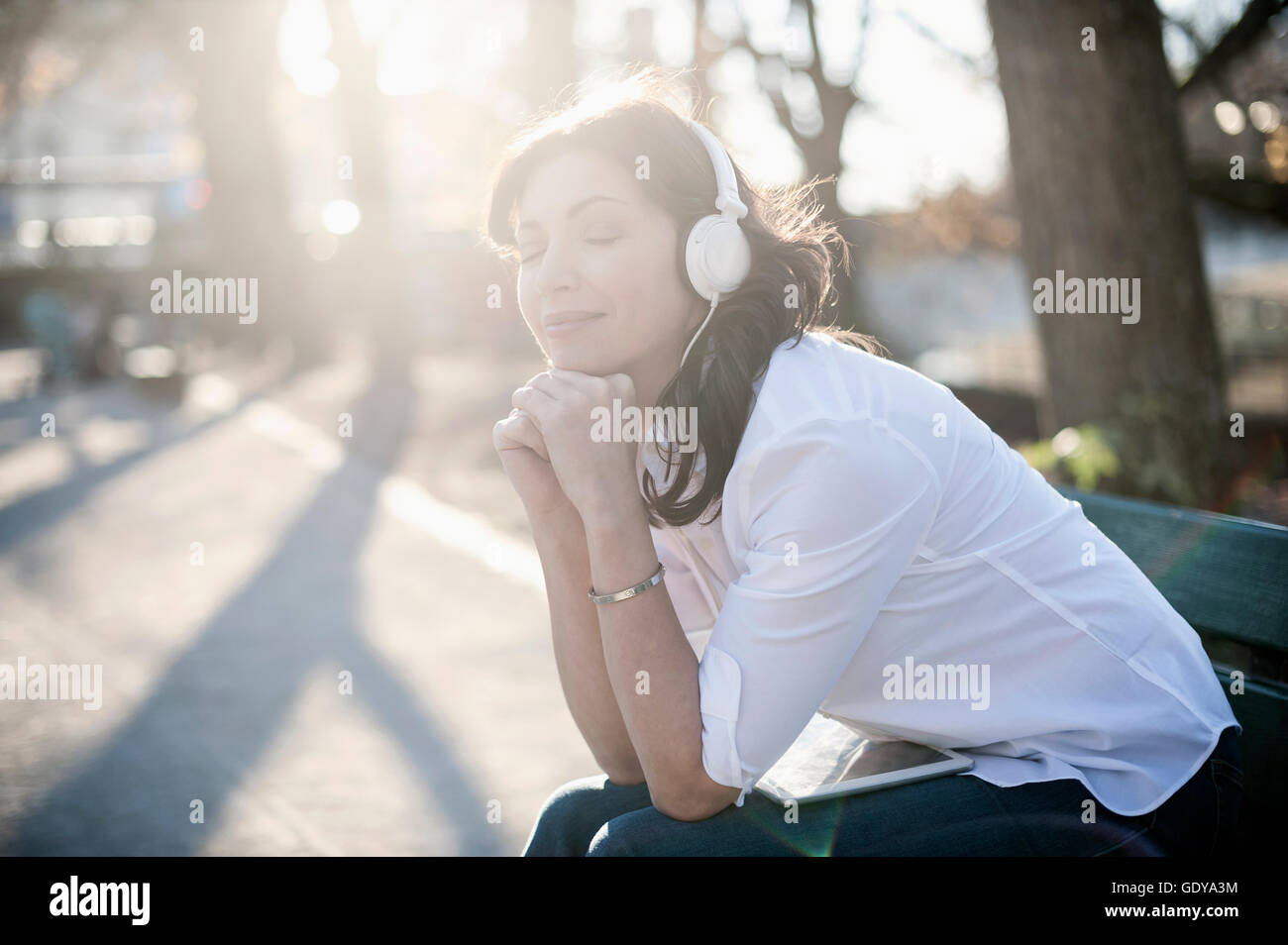 Reife Frau Musikhören und sitzen in der Park Bench, Bayern, Deutschland Stockfoto