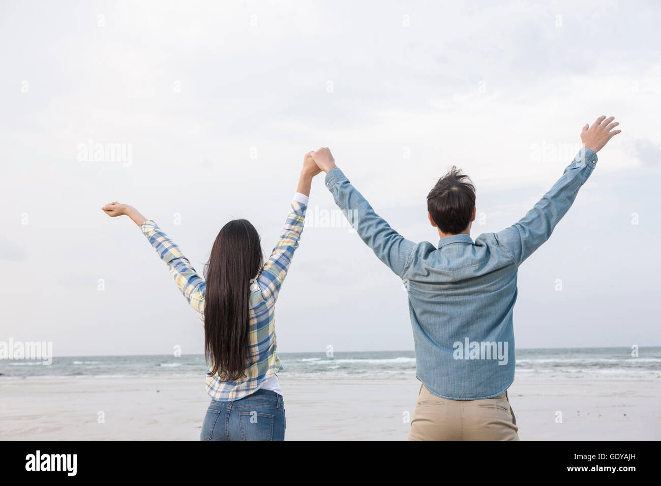 Rückseite des jungen Paares stehend Arme gegen Strand Stockfoto