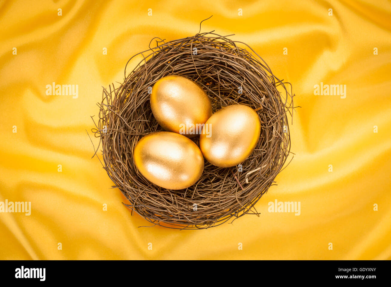 Drei goldenen Eiern in einem Nest auf gelben Seidentuch Stockfoto