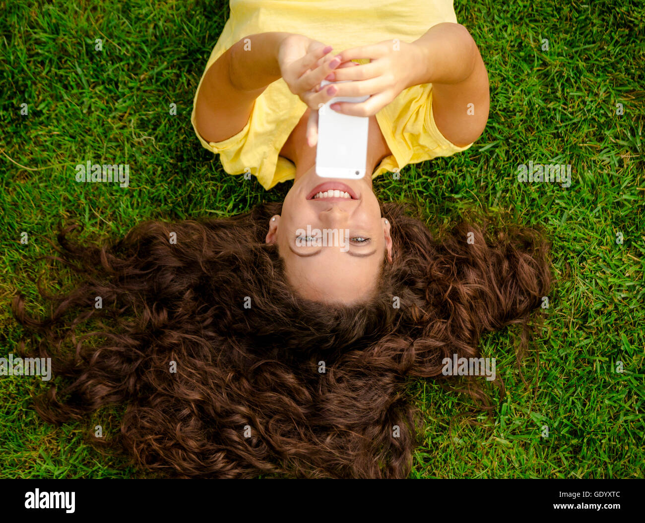 Lächelnde junge Frau auf dem Rasen liegen und ein Selbstporträt zu machen Stockfoto