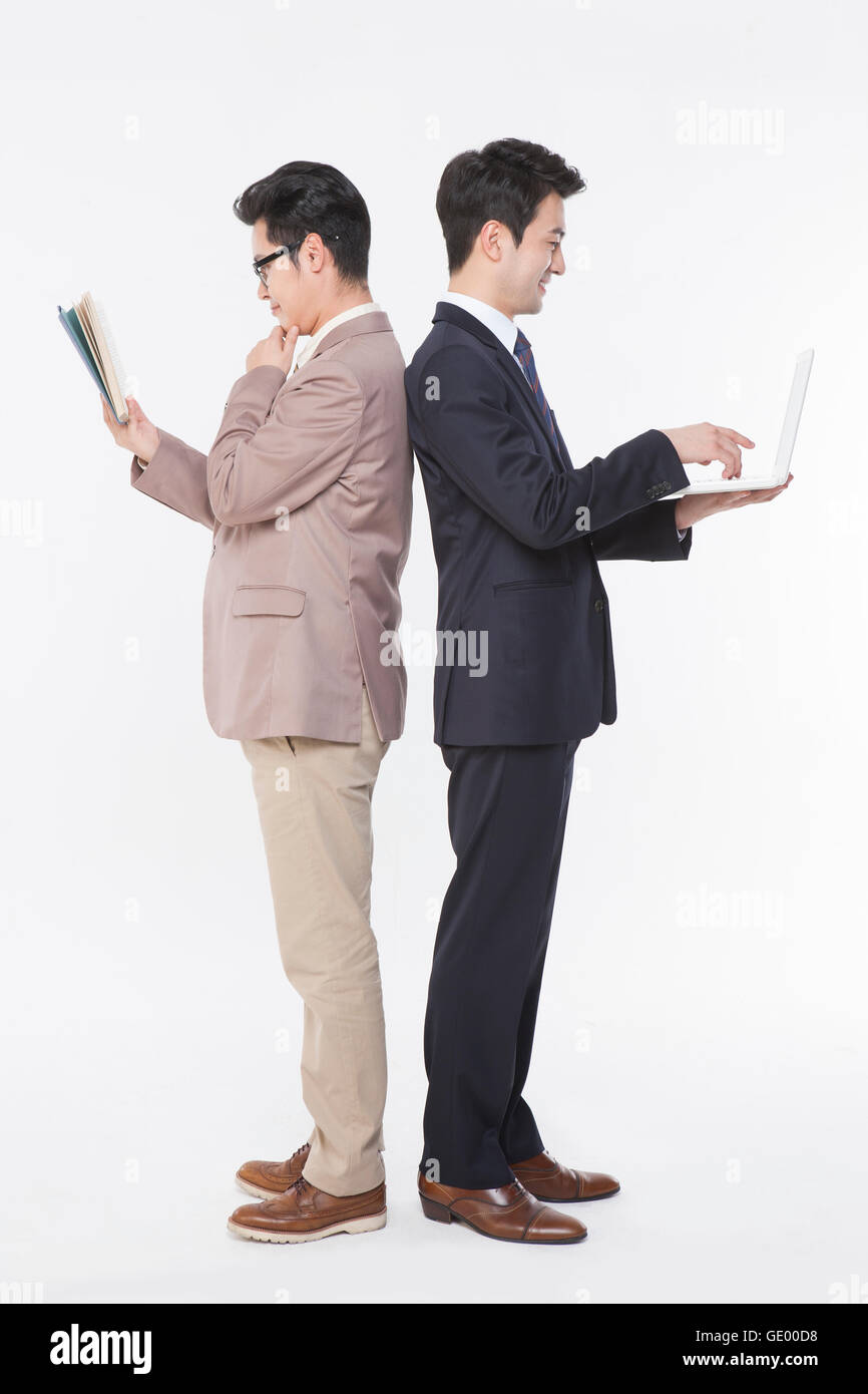 Seitenansicht der Geschäftsmann lesen ein Buch und ein weiteres mit einem Notebookcomputer stehen Rücken an Rücken Stockfoto