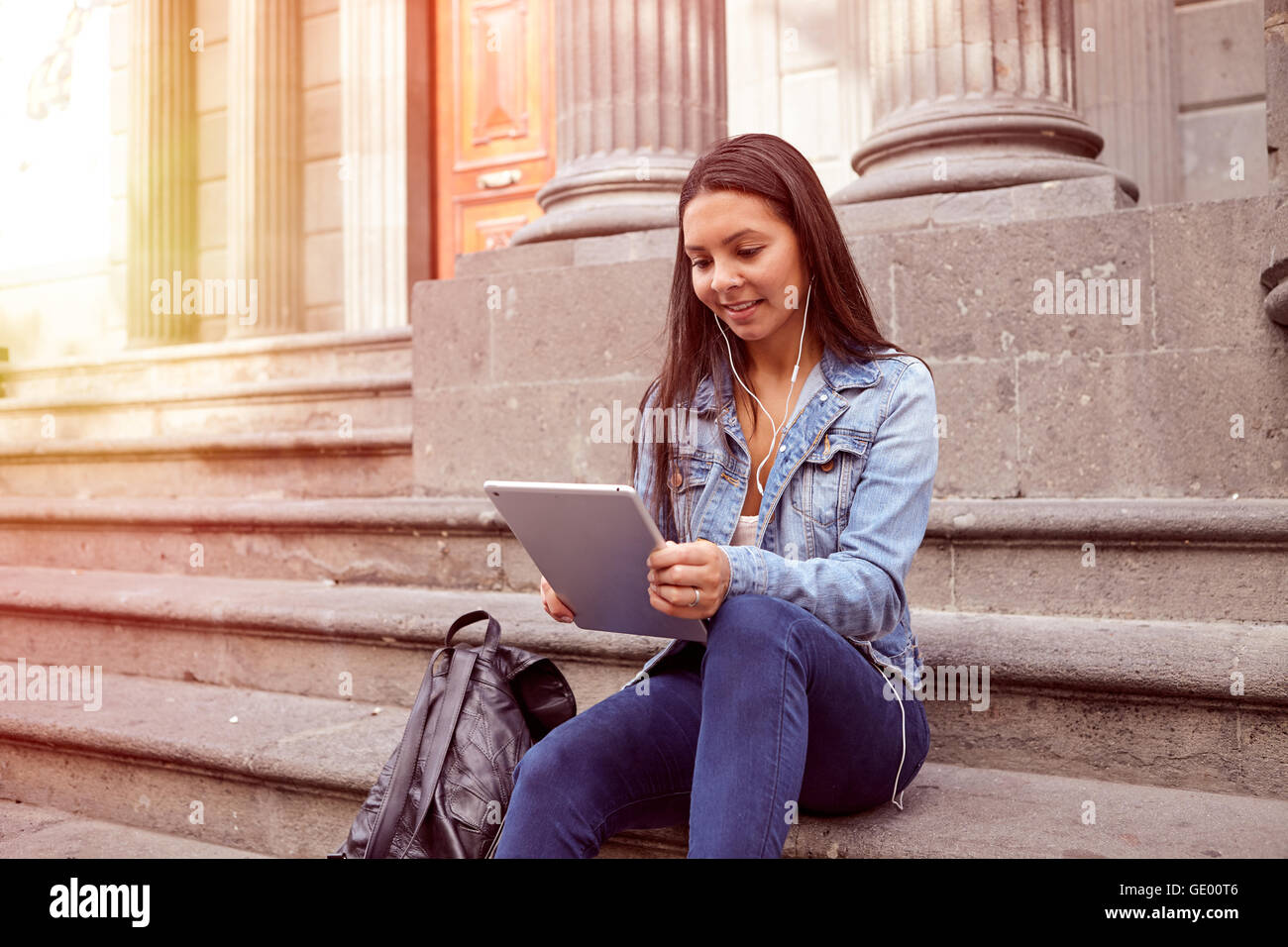 Hübsches junges Mädchen Blick auf ihr Tablet beim Sitzen auf den Stufen von einem alten Gebäude Lächeln auf den Lippen tragen ihre Haare locker und lässig Stockfoto