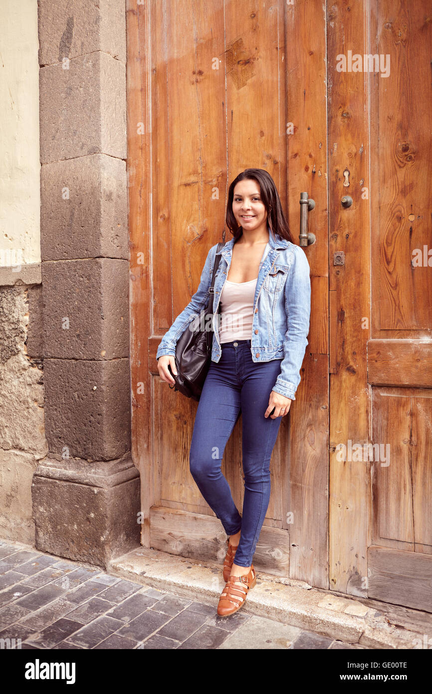 Hübsches junges Mädchen schaut in die Kamera während an alten Holztüren, Lächeln und ihre Haare locker in Jeans und Denim Jac gelehnt Stockfoto