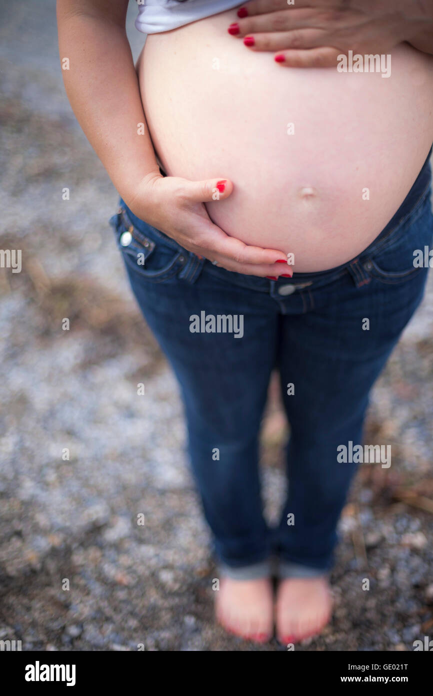 Schwangere Frau mit Händen auf Magen am Steinstrand, Ammersee, Upper Bavaria, Bavaria, Germany Stockfoto