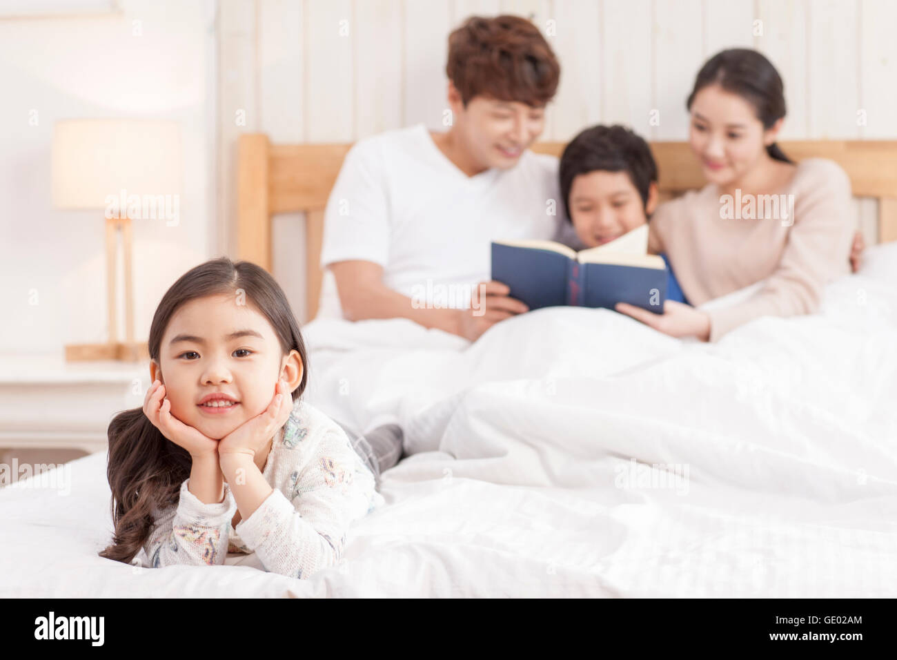 Porträt eines lächelnden Mädchens mit Vater, Sohn und Mutter ein Buch hinter ihr in einem Bett Stockfoto