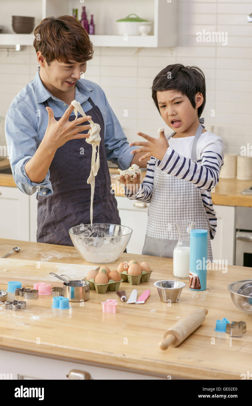 Lächelnden Vater hält Teig und Sohn mit einem Stirnrunzeln in Küche Stockfoto