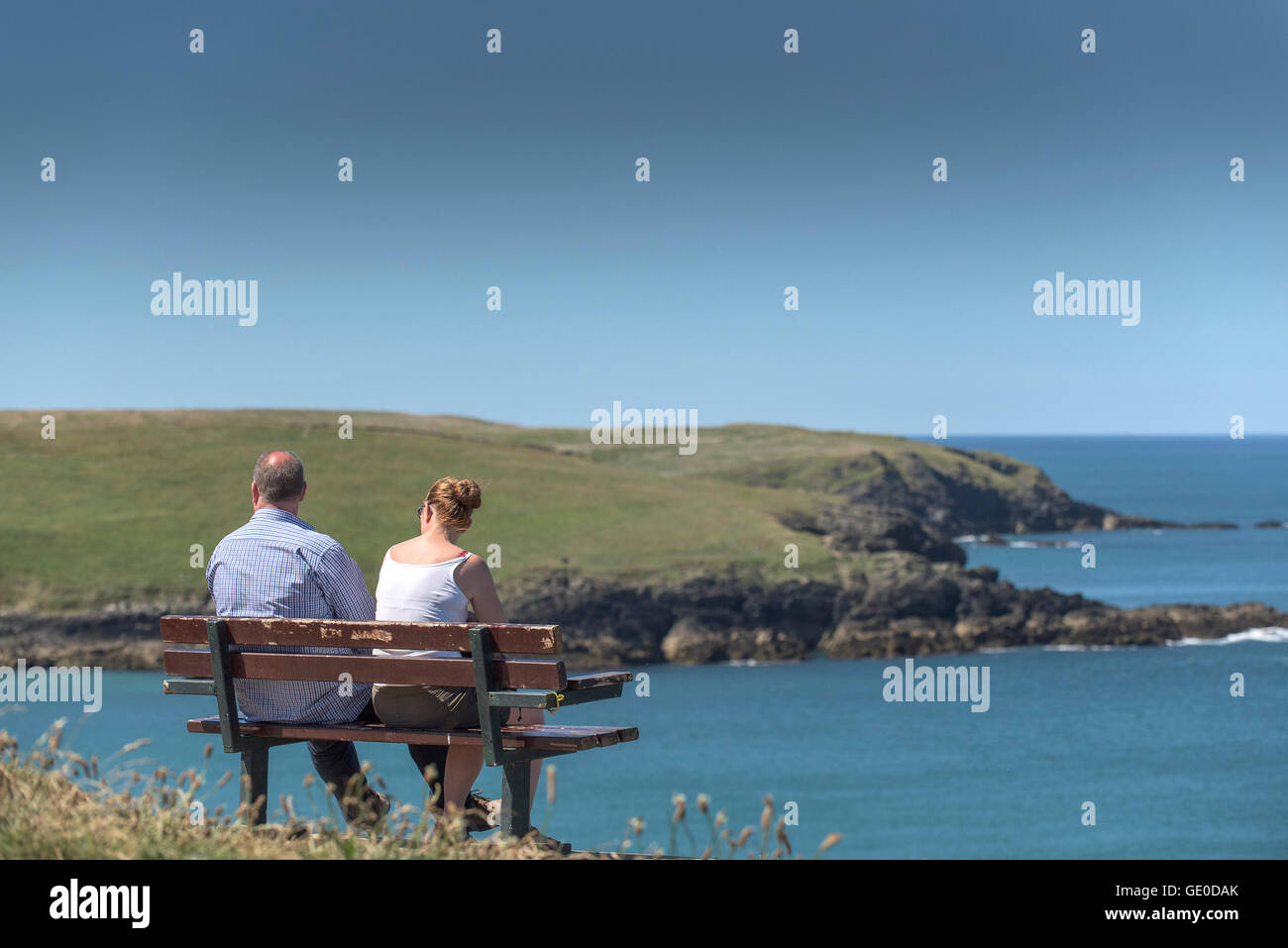 Touristen entspannen Sie auf einer Bank und mit Blick auf West Pentire Landzunge in Newquay, Cornwall. Stockfoto