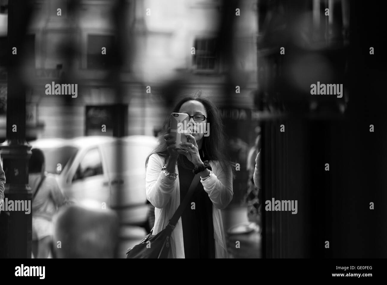 Eine Frau nimmt ein Foto auf dem Trafalgar Square. Betrachtet durch die Gitterstäbe einen u-Bahn-Eingang Stockfoto