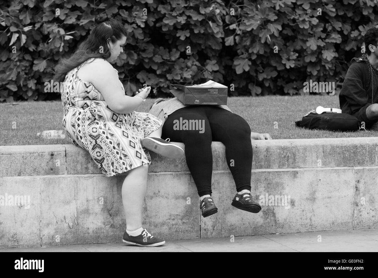 Zwei Frauen entspannen am Trafalgar Square in London, England. Ein Blick auf ihr mobiles Gerät, eine Einkaufstasche ruht auf der anderen. Stockfoto