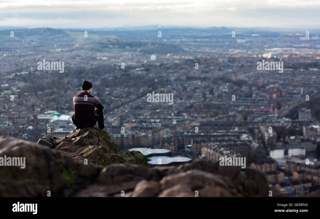 Mann trägt einen Hut mit Blick auf Edinburgh Stadt im Winter von einer Klippe auf Arthurs Sitz Stockfoto