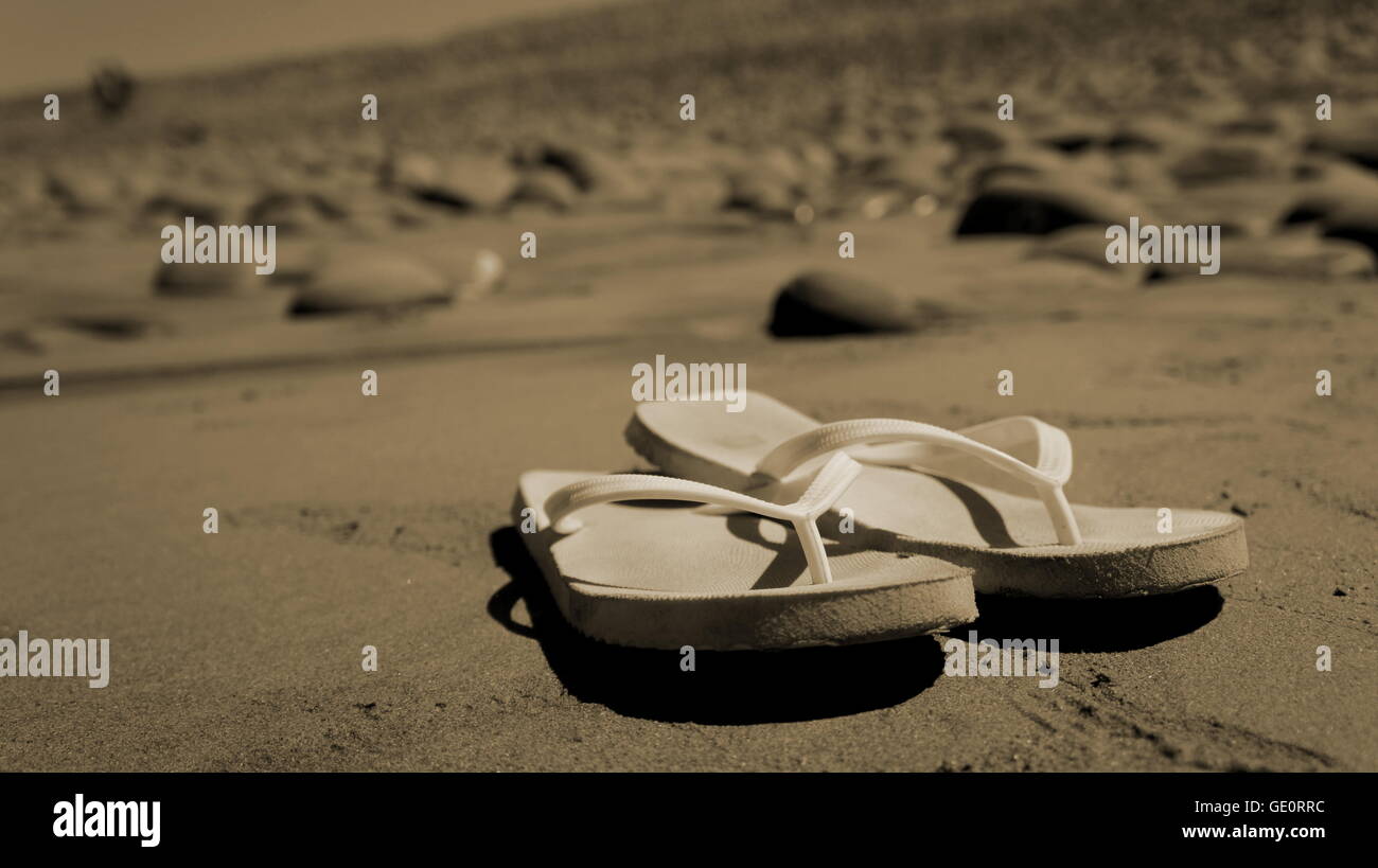 weißen Flip-Flops am Sandstrand mit Felsen im Hintergrund Stockfoto