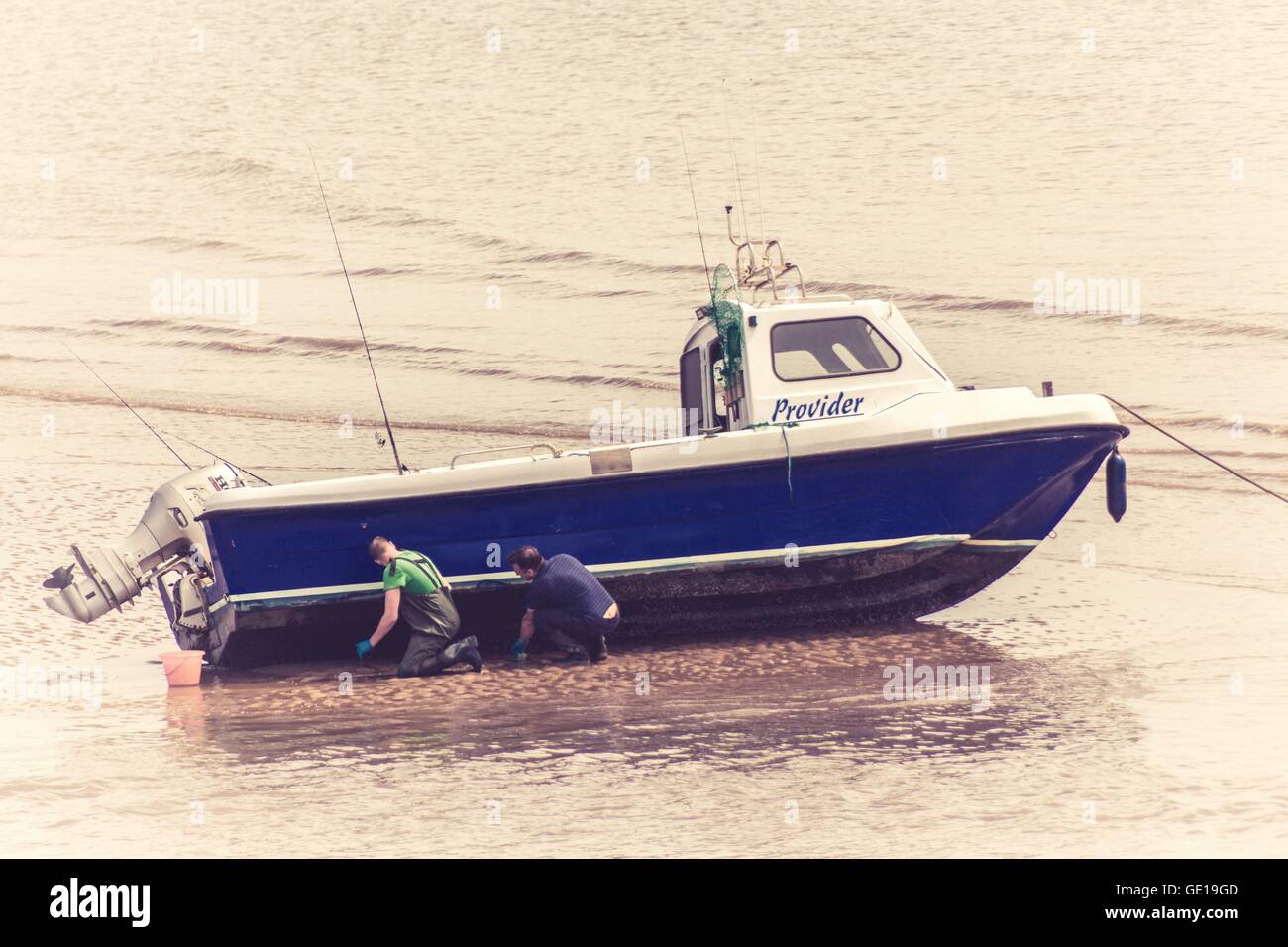 Aufgenommen während Juli 2016 am Strand von Porthcawl zweier Männer, die ihr Boot am Strand zu reparieren, bevor die Flut kommt. Stockfoto
