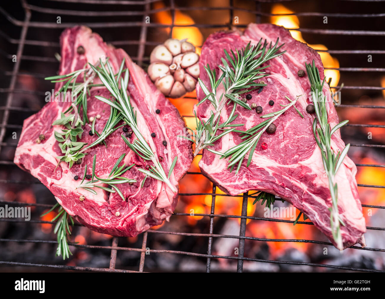 Rib-Eye-Steaks und Grill mit brennendem Feuer hinter ihnen. Stockfoto