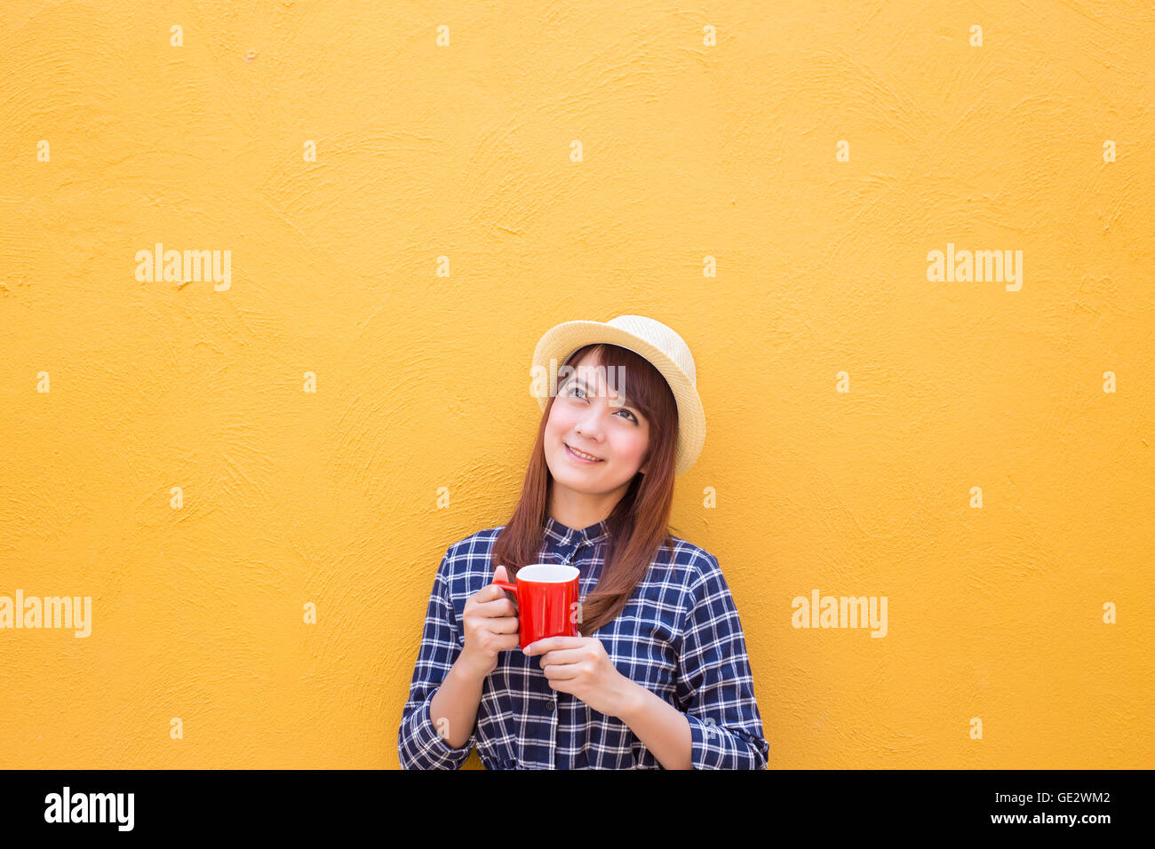 lächelnde Frau Verschleiß in Kleid und Hut hält rote Kaffeetasse auf gelben Zement Wand Hintergrund, denken, Phantasie Stockfoto