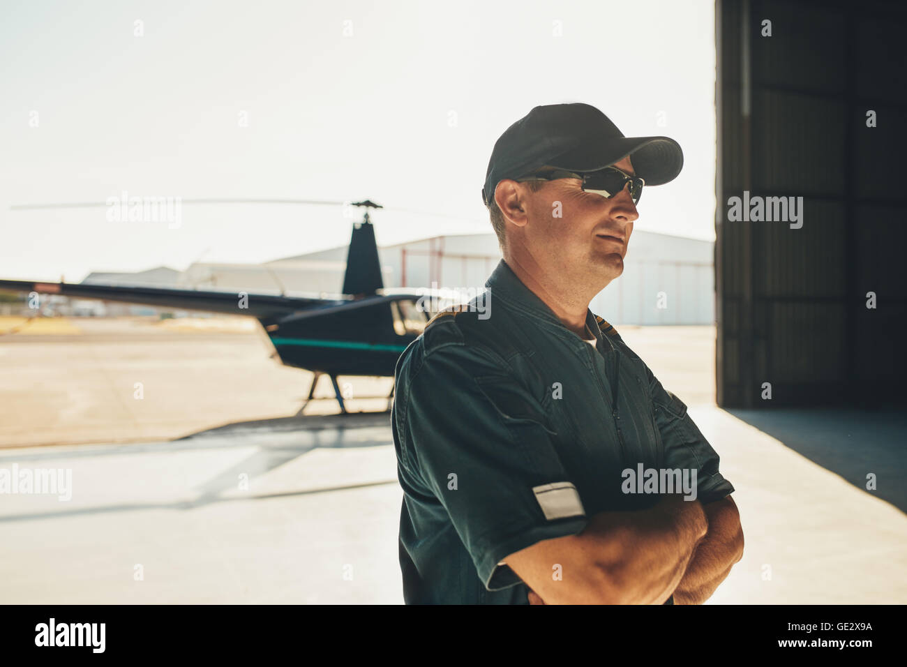 Porträt der Hubschrauberpilot in einheitlichen Stand mit seine Arme verschränkt und wegschauen mit einem Hubschrauber im Hintergrund Stockfoto