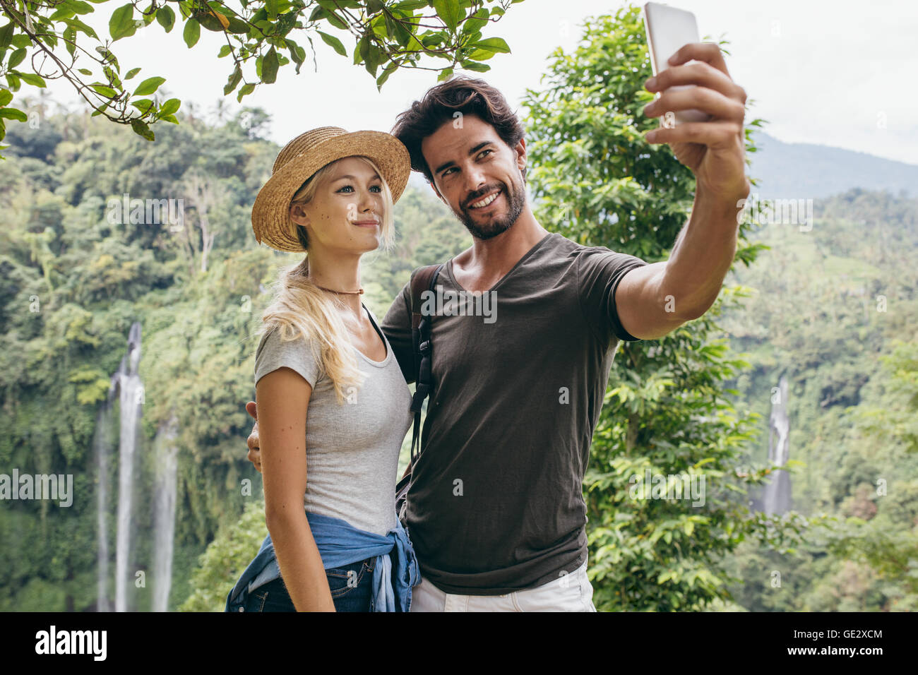 Junges Liebespaar unter Selbstbildnis mit Wasserfall im Hintergrund. Mann und Frau im Urlaub im Wald nehmen Selfie mit th Stockfoto