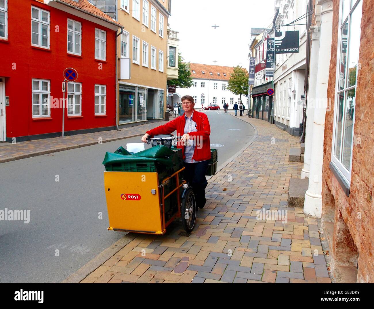 Junge, weibliche Postarbeiter stand neben ihrem Post Fahrrad auf einer Straße in Dänemark. Gebäuden umgeben. Stockfoto