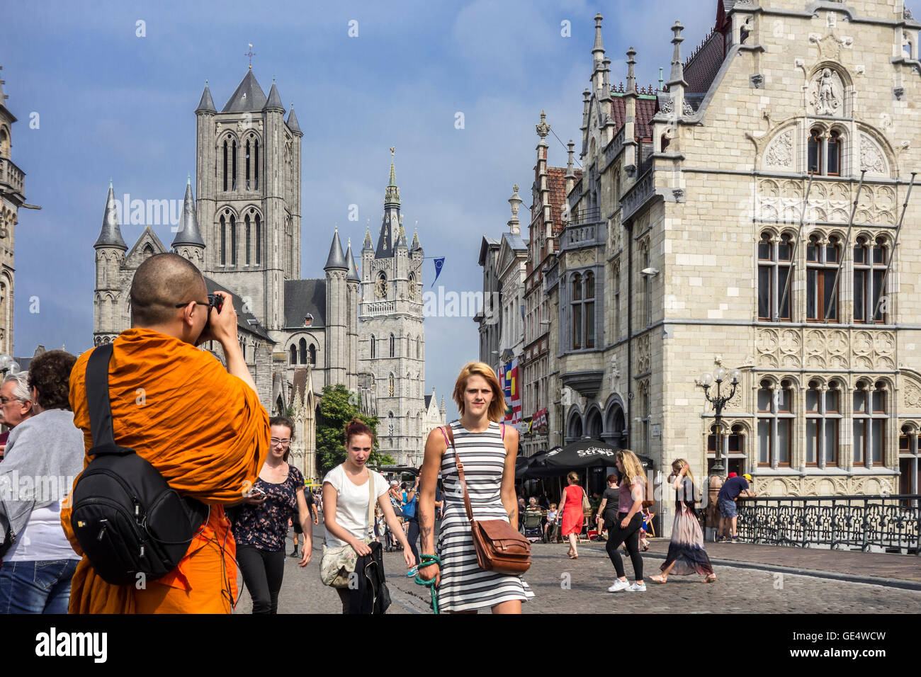 Buddhistischer Mönch gekleidet in orange Gewand, die Bilder von der St.-Nikolaus Kirche und der Glockenturm in der Stadt Gent, Belgien Stockfoto