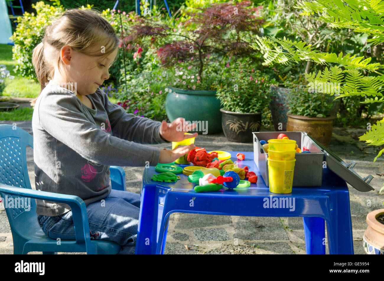 Drei Jahre alten Mädchen spielen mit Play-Doh Modellierung Kitt. VEREINIGTES KÖNIGREICH. Draußen im Garten. Stockfoto