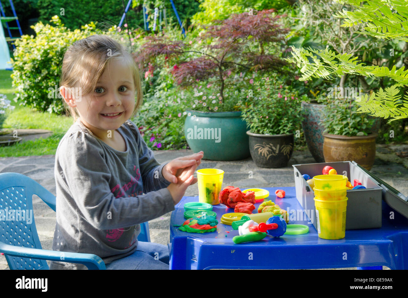 Drei Jahre alten Mädchen spielen mit Play-Doh Modellierung Kitt. VEREINIGTES KÖNIGREICH. Draußen im Garten. Stockfoto