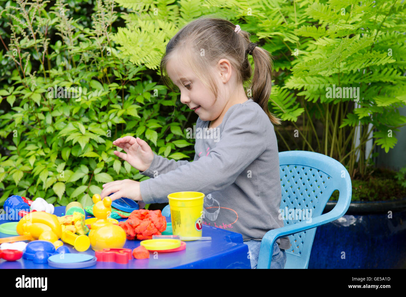 Drei Jahre alten Mädchen spielen mit Play-Doh Modellierung Kitt. VEREINIGTES KÖNIGREICH. Draußen im Garten. Stockfoto