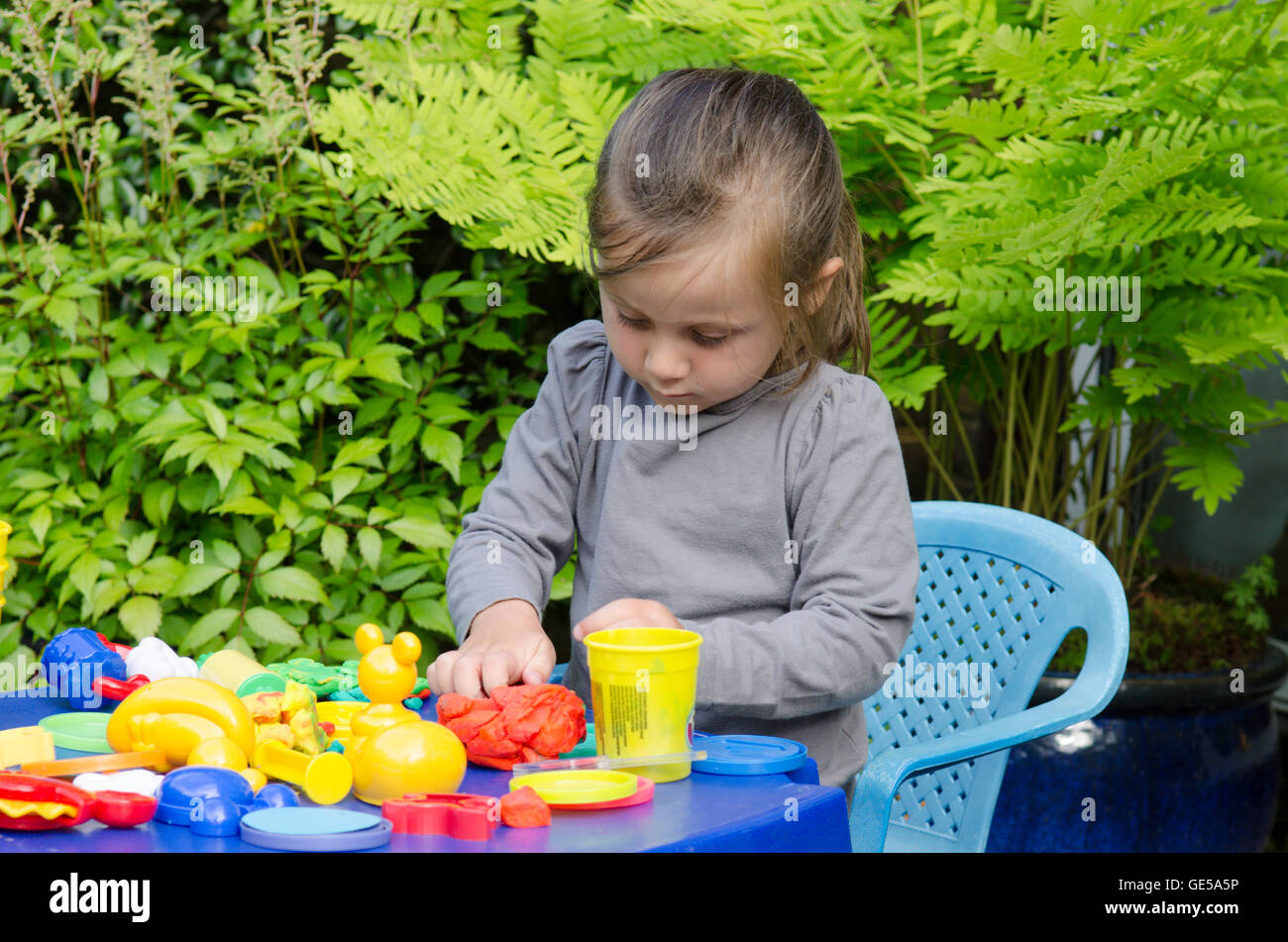 Drei Jahre alten Mädchen spielen mit Play-Doh Modellierung Kitt. VEREINIGTES KÖNIGREICH. Draußen im Garten. Stockfoto