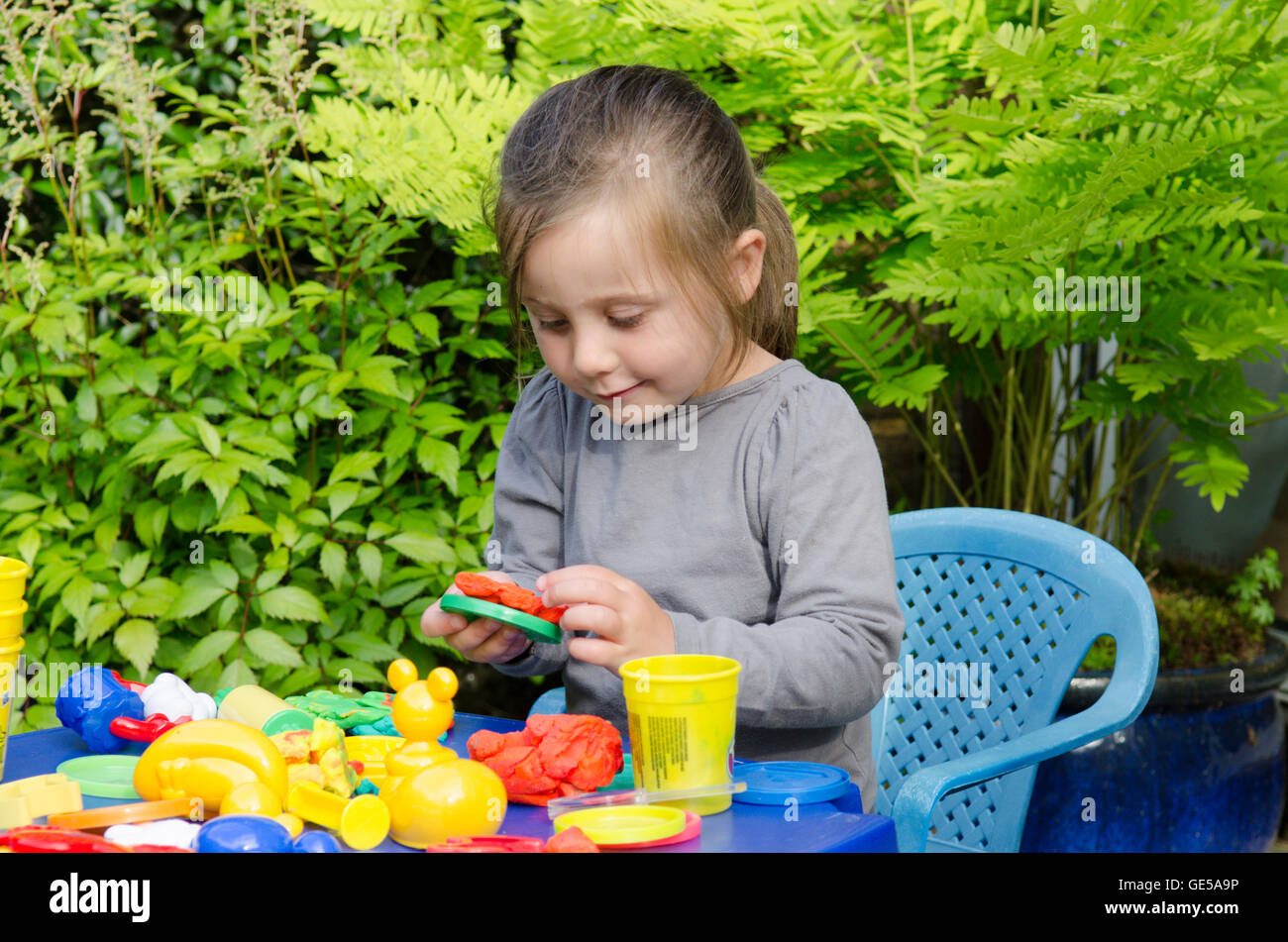 Drei Jahre alten Mädchen spielen mit Play-Doh Modellierung Kitt. VEREINIGTES KÖNIGREICH. Draußen im Garten. Stockfoto