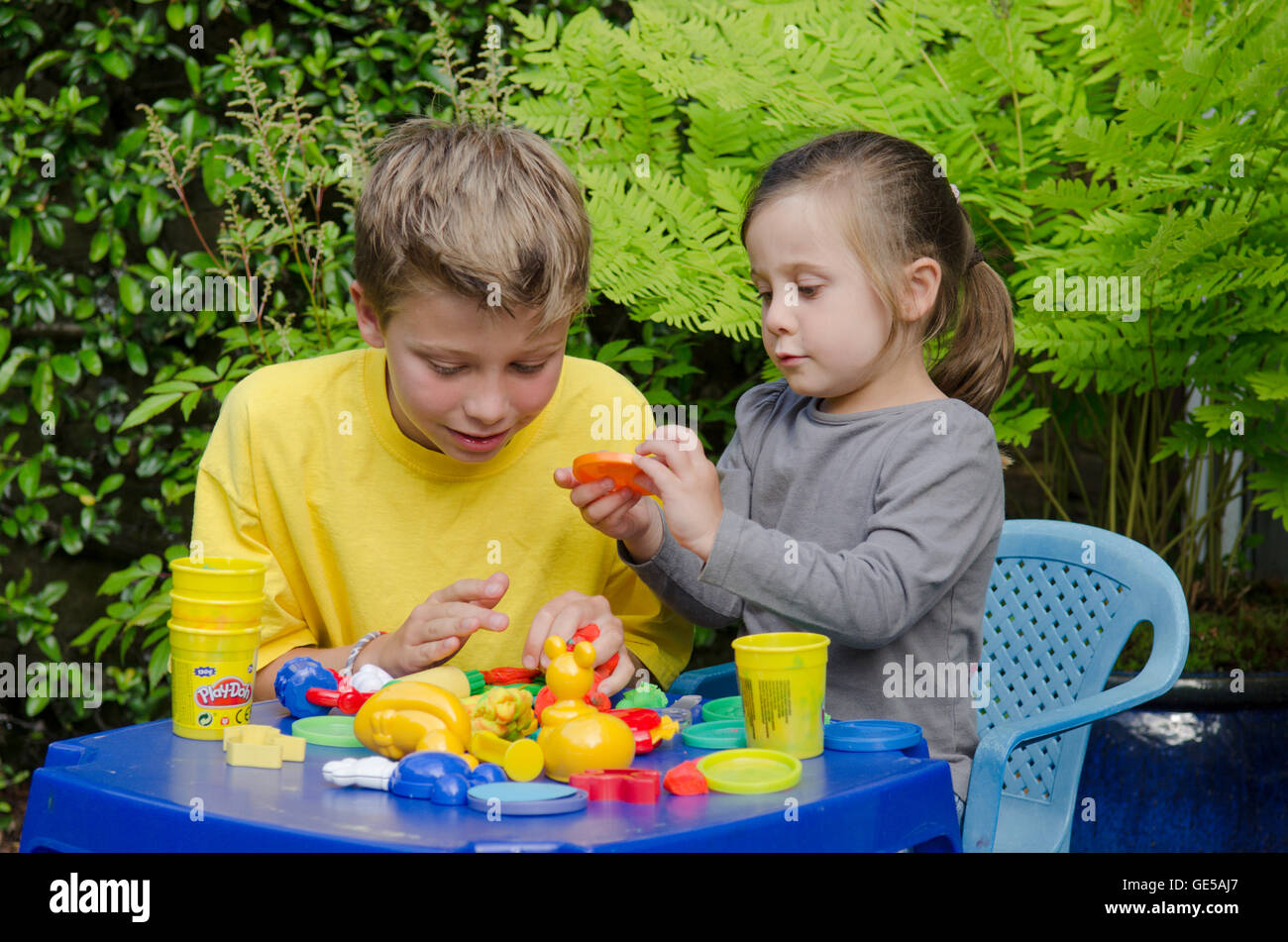 Drei Jahre alten Mädchen und Ten-Year-Old Boy, Bruder und Schwester, spielen mit Play-Doh Modellierung Kitt. VEREINIGTES KÖNIGREICH. Draußen im Garten. Stockfoto