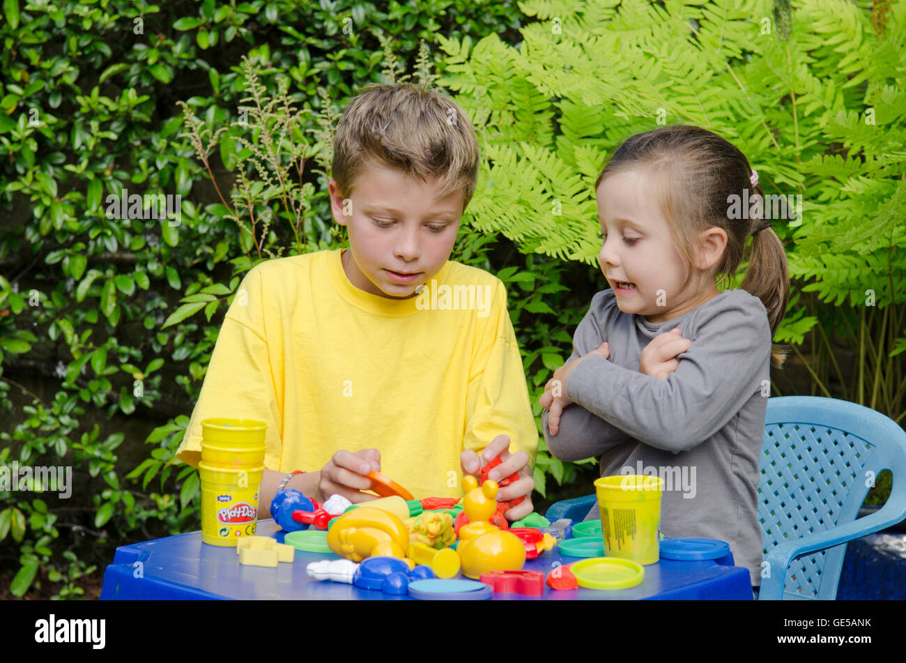 Drei Jahre alten Mädchen und Ten-Year-Old Boy, Bruder und Schwester, spielen mit Play-Doh Modellierung Kitt. VEREINIGTES KÖNIGREICH. Draußen im Garten. Stockfoto