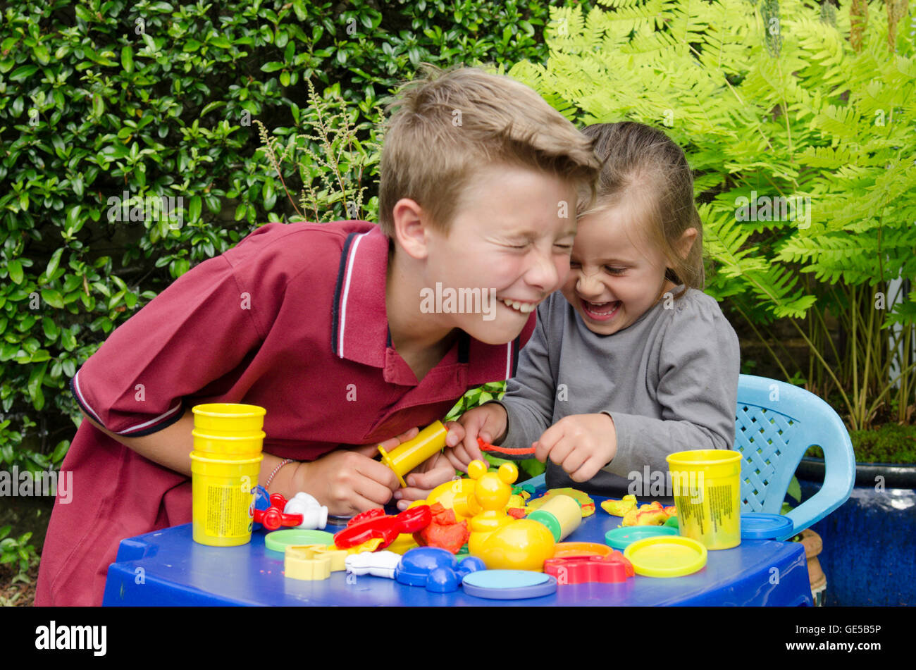 Drei Jahre alten Mädchen und Ten-Year-Old Boy, Bruder und Schwester, spielen mit Play-Doh Modellierung Kitt. VEREINIGTES KÖNIGREICH. Draußen im Garten. Stockfoto