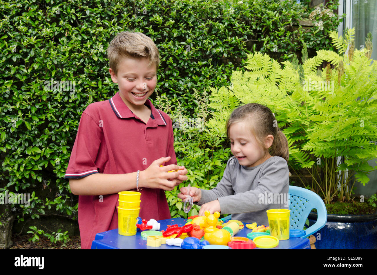 Drei Jahre alten Mädchen und Ten-Year-Old Boy, Bruder und Schwester, spielen mit Play-Doh Modellierung Kitt. VEREINIGTES KÖNIGREICH. Draußen im Garten. Stockfoto