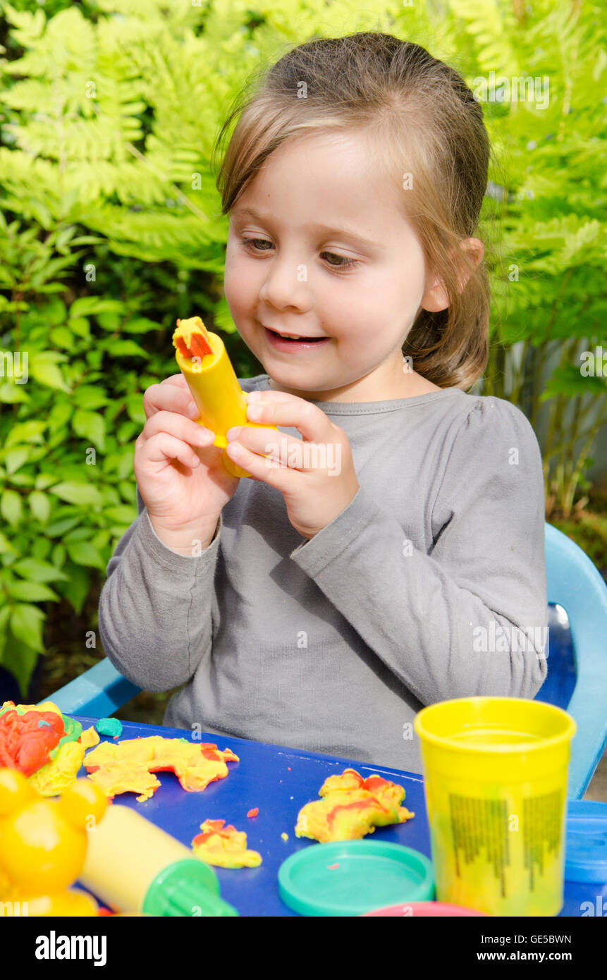 Drei Jahre alten Mädchen spielen mit Play-Doh Modellierung Kitt. VEREINIGTES KÖNIGREICH. Draußen im Garten. Stockfoto